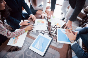 Diverse group of professionals gathered around table filled with charts and graphs.